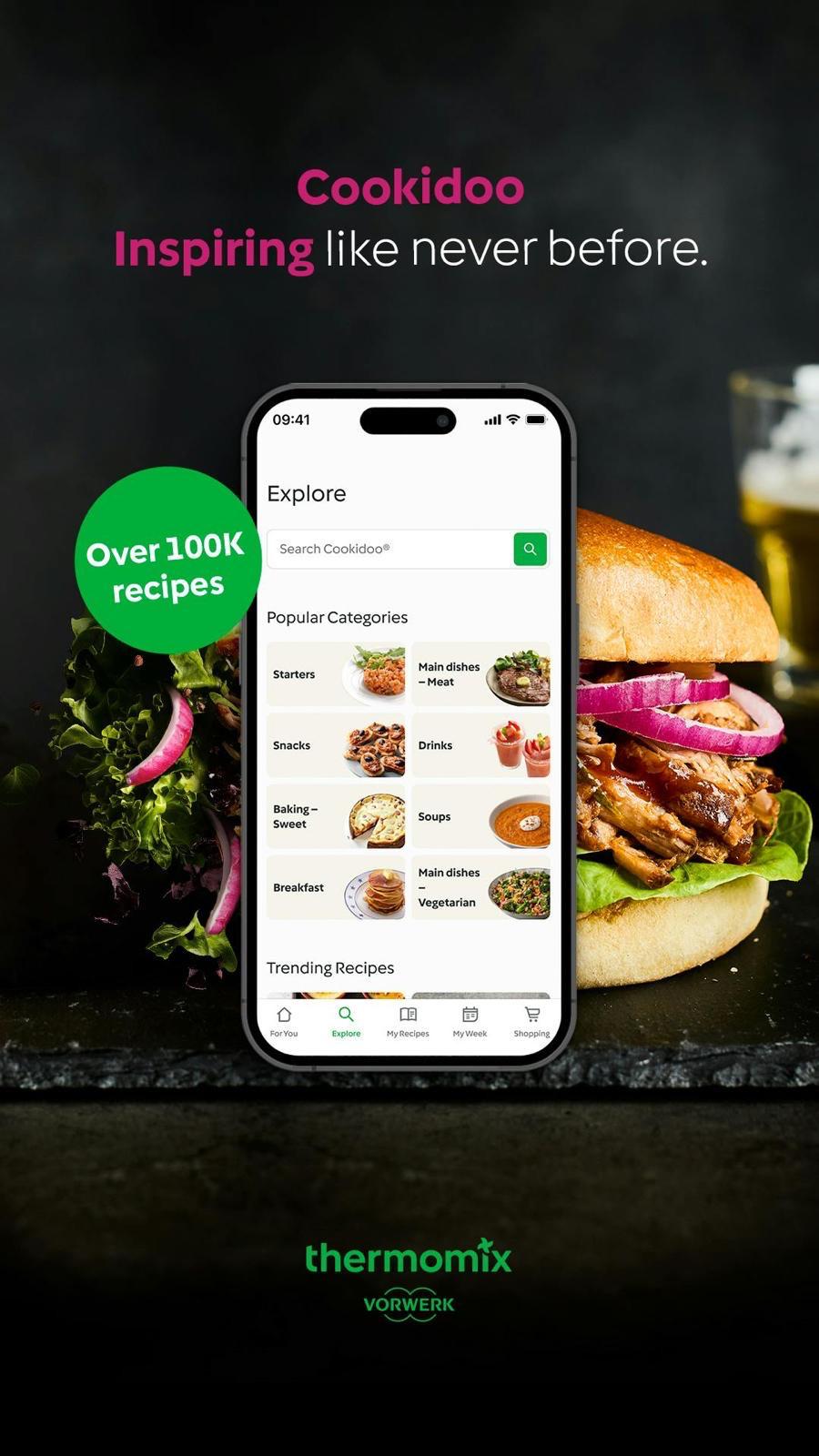Cookidoo app on a phone with popular recipe categories and a burger in the background